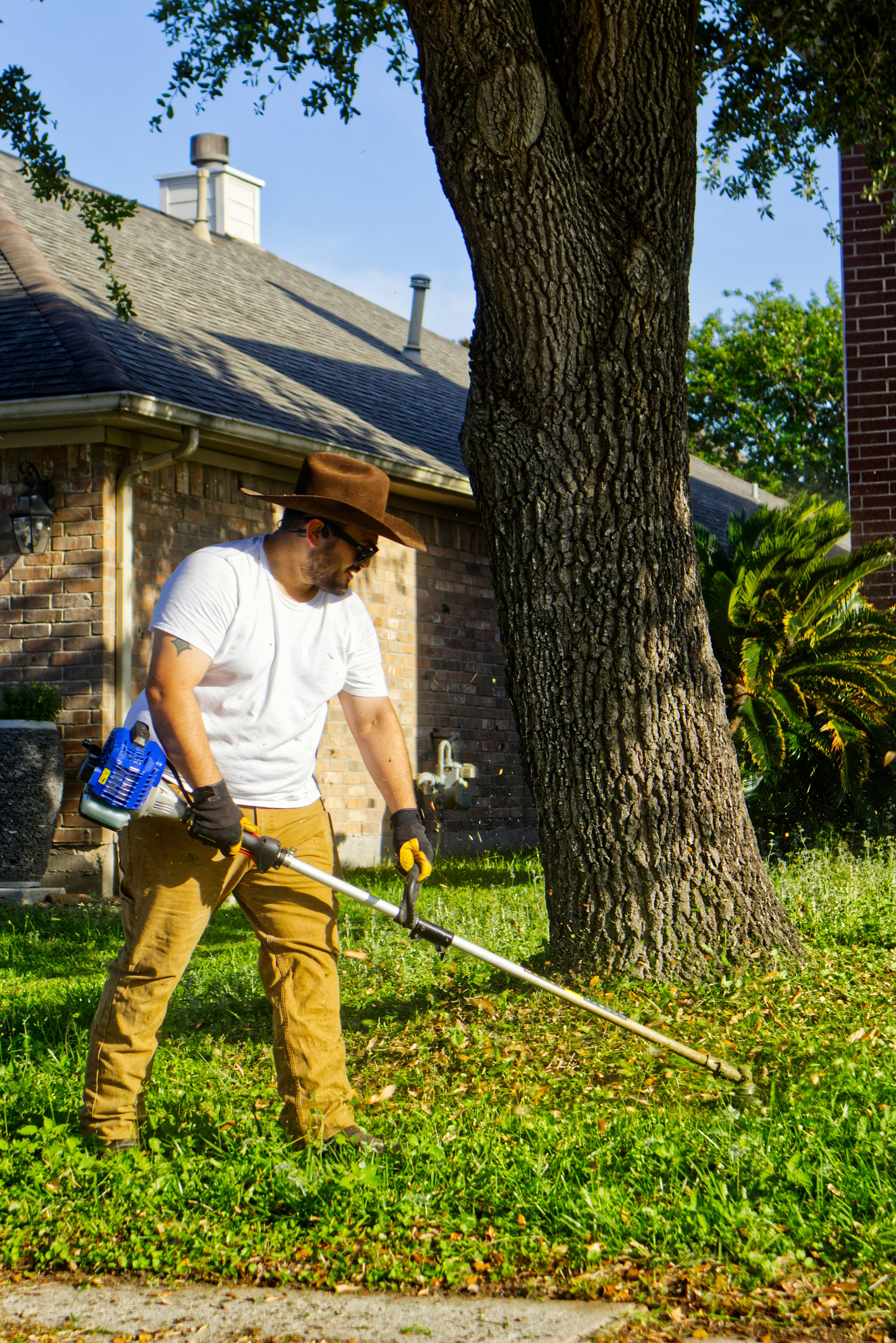 A landscaper using a string trimmer in a residential yard.