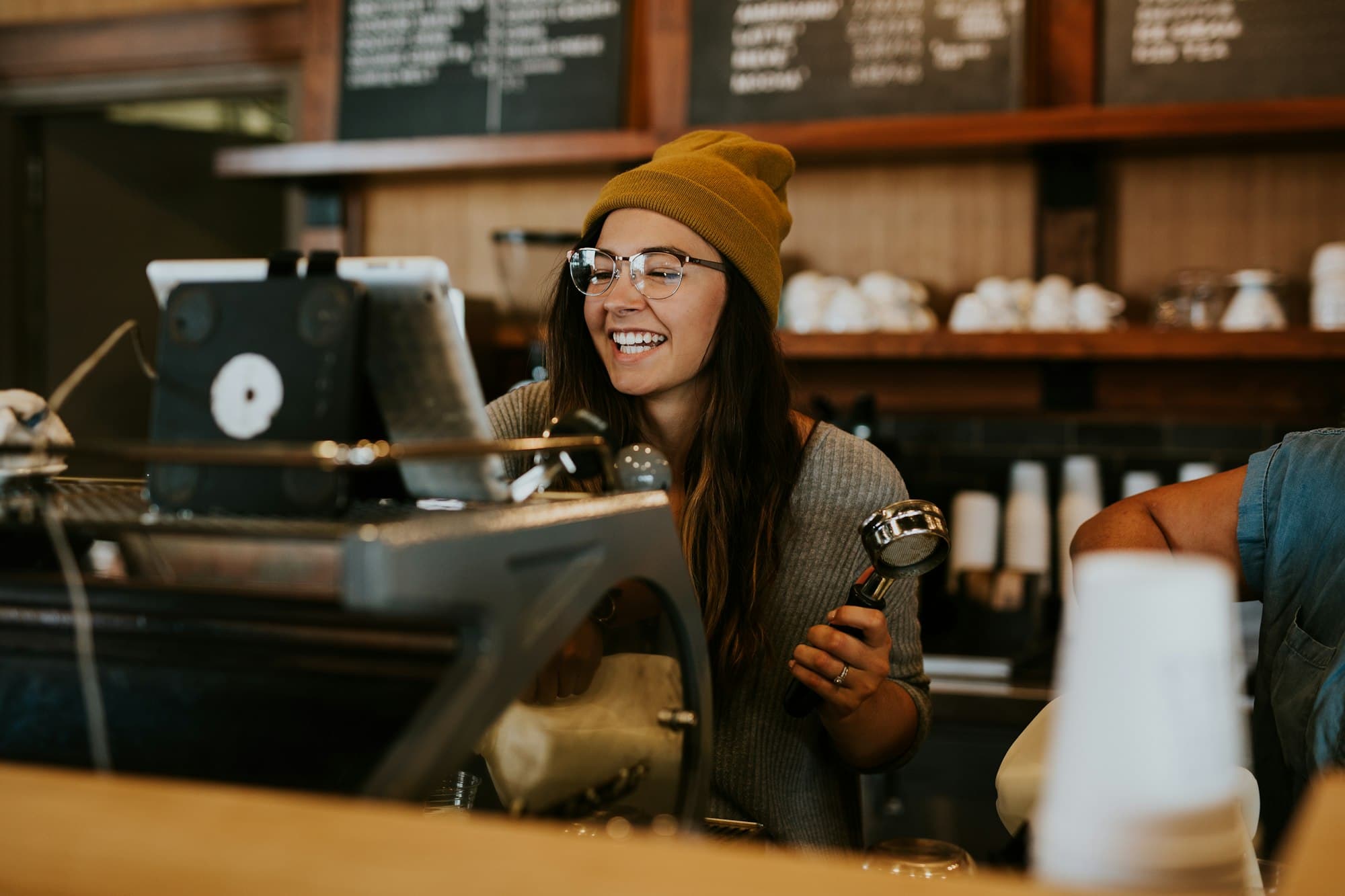A barista smiling behind the espresso machine, with menu boards on the wall behind her.