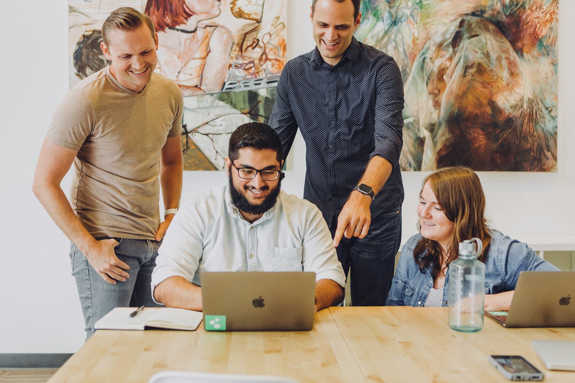 A corporate team gathered around a laptop at a shared table.