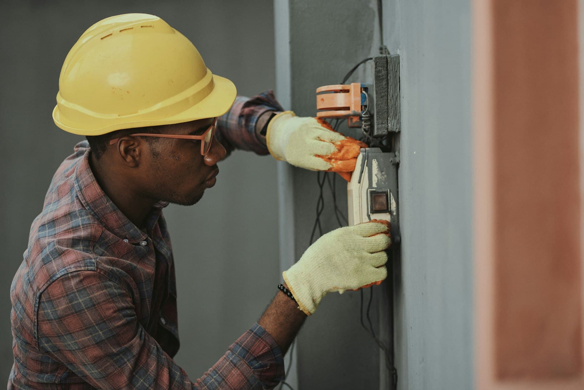 An electrician in a hard hat testing wiring at a panel.