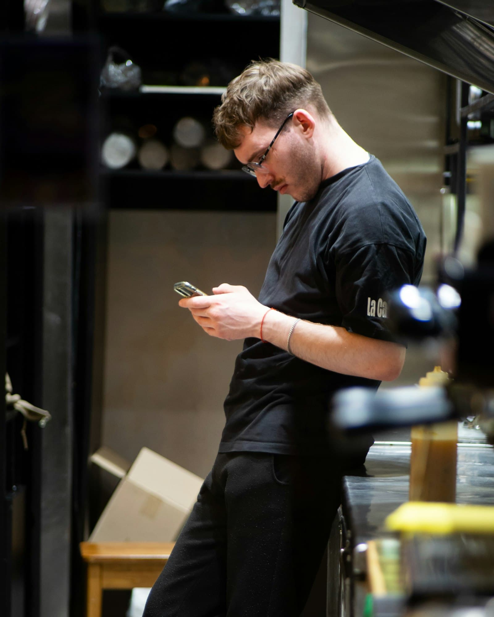 A GM in a black shirt checks his phone in the kitchen.