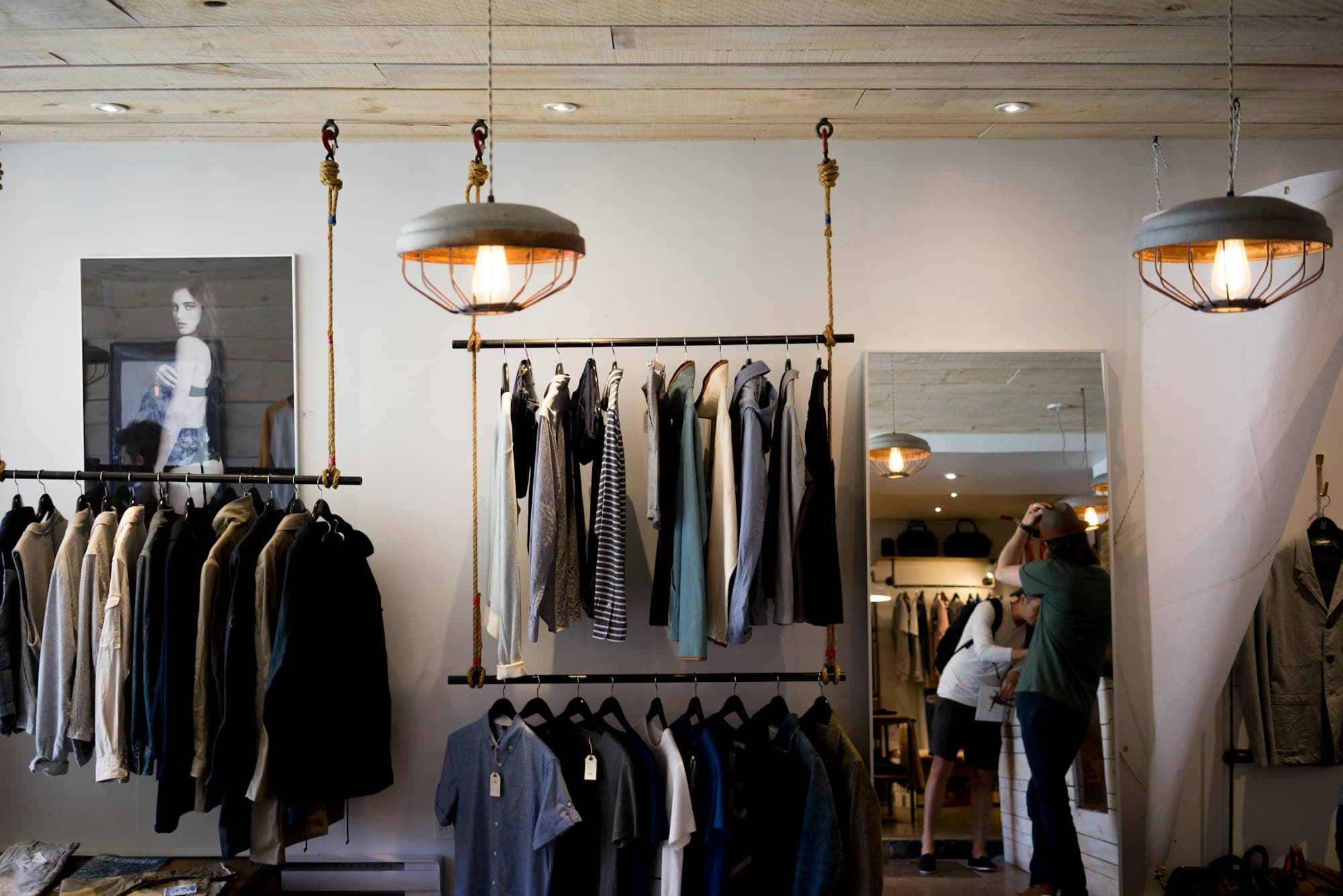 A clothing boutique with garments on hanging racks and a shopper at the mirror.